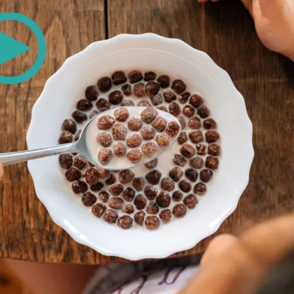 Photograph of a child at a wooden table with chocolate cereal on a spoon, taken from above