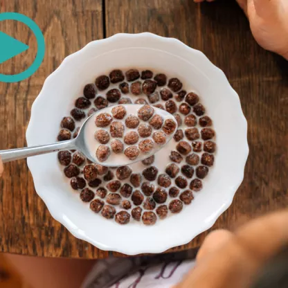 Photograph of a child at a wooden table with chocolate cereal on a spoon, taken from above 