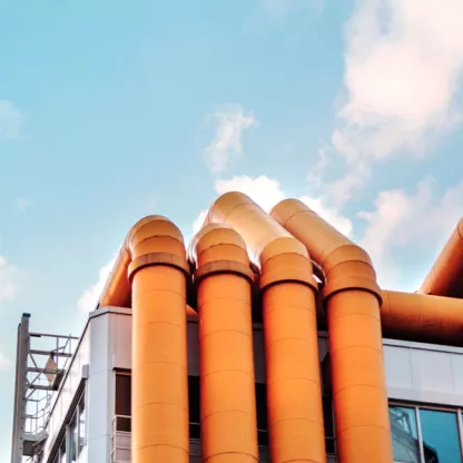 Industrial architecture with orange pipe structure against a cloudy blue sky.